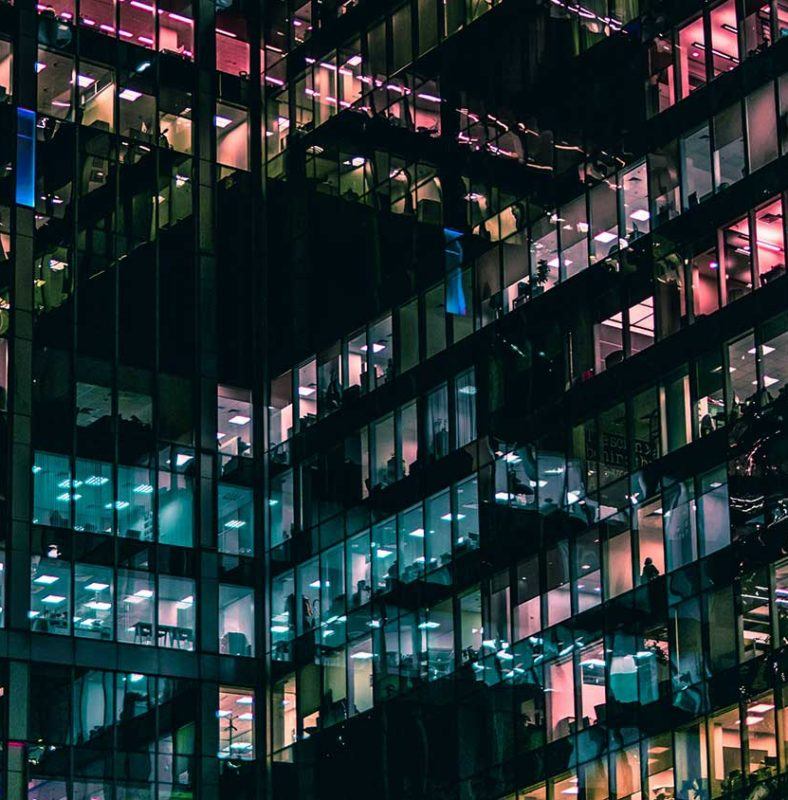 the exterior of an office building at night with different color lights in different windows